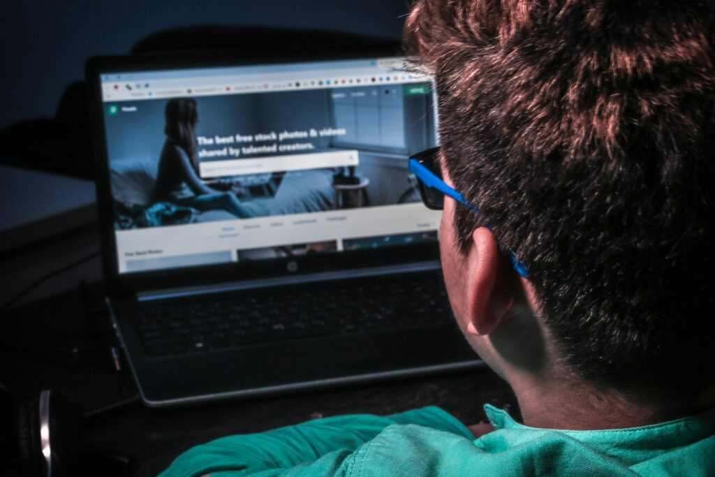 Close-up of a person using a laptop to browse stock photos online in dim lighting.